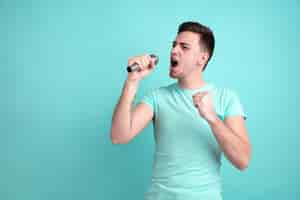 Foto gratuita cantando como una estrella. retrato de joven caucásico aislado en la pared azul. hermoso modelo masculino de estilo casual, colores pastel. concepto de emociones humanas, expresión facial.