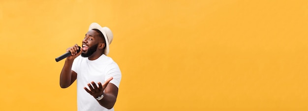 Canto afroamericano hermoso joven del muchacho emocional con el micrófono aislado en fondo amarillo