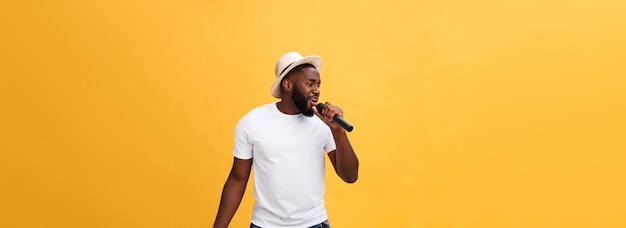 Canto afroamericano hermoso joven del muchacho emocional con el micrófono aislado en fondo amarillo