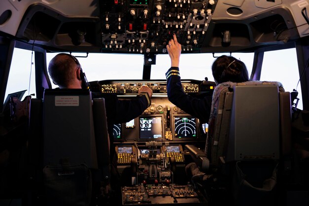 Capitán y mujer copiloto preparándose para volar en avión y despegar con navegación en el tablero al mando de la cabina. La tripulación de la aerolínea fija el nivel de altitud y con los botones del panel de control, vuela el avión.