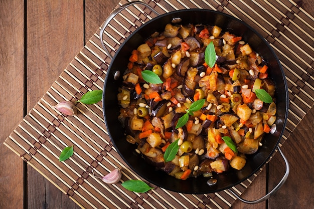 Caponata italiana con sartén sobre una mesa de madera