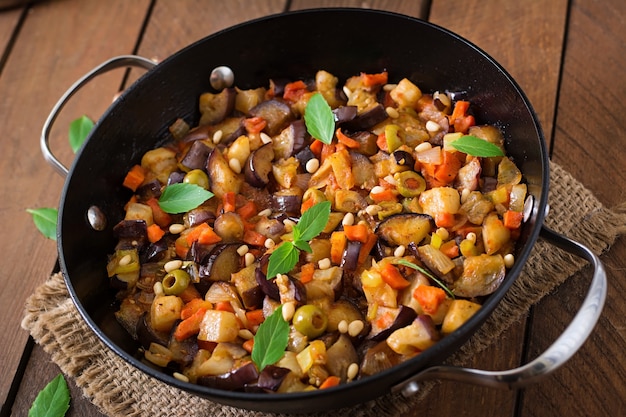 Caponata italiana con sartén sobre una mesa de madera