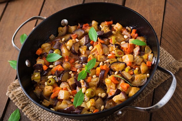 Caponata italiana con sartén sobre una mesa de madera