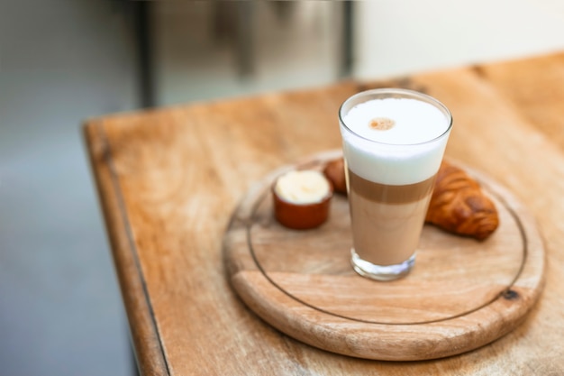 Cappuccino en vaso con croissant en bandeja circular de madera