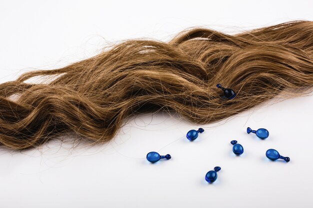 Cápsulas azules con vitaminas para el cabello se encuentran en los rizos de cabello castaño