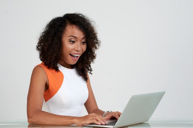 Captura de cintura de mujer asiática sentada en el escritorio entusiasmada por la información de la pantalla del portátil