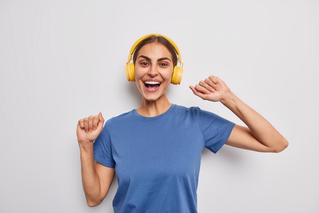 Captura interior de una joven positiva y despreocupada que sacude los brazos y se mueve con el ritmo de la música se ríe alegremente escucha música a través de auriculares inalámbricos aislados sobre fondo blanco capta cada parte de la canción