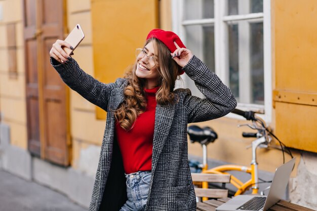 Captura de mujer con peinado rizado con smartphone mientras hace selfie cerca de casa