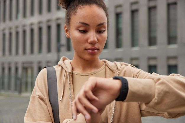 Captura recortada de un modelo de fitness serio que mira los resultados de las comprobaciones del dispositivo de reloj inteligente digital después de entrenar en el gimnasio, usa una sudadera beige informal y hace ejercicio regularmente al aire libre. Motivación del deporte de la gente