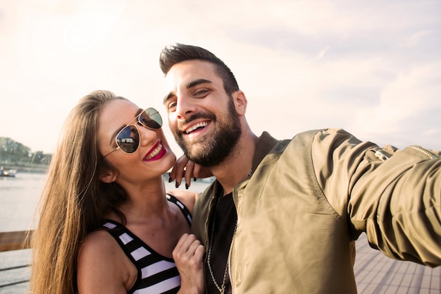 Foto gratuita capturando momentos brillantes. pares amorosos jovenes alegres que hacen el selfie en la cámara mientras que se coloca al aire libre.