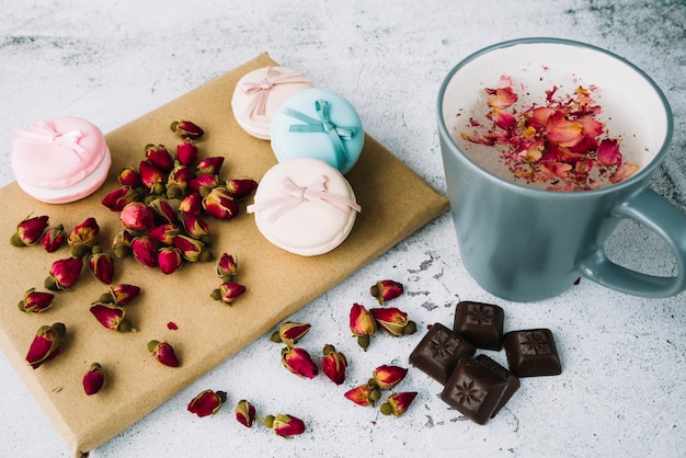 Capullos de rosa secos; macarrones y piezas de chocolate a bordo con taza