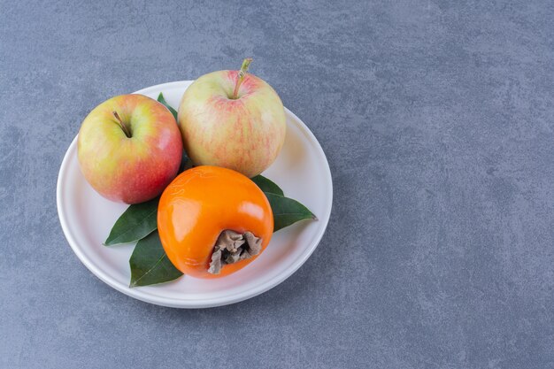 Caqui y manzanas en placa sobre mesa de mármol.