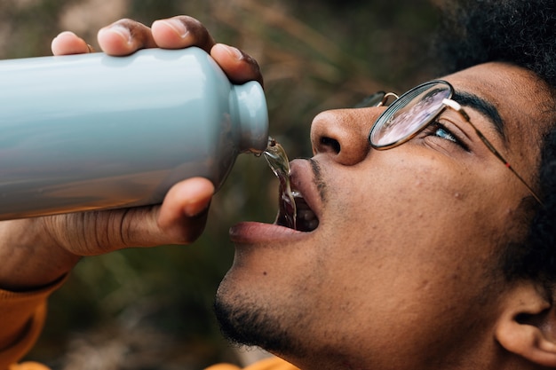 Foto gratuita cara de excursionista masculino con anteojos bebiendo el agua de la botella