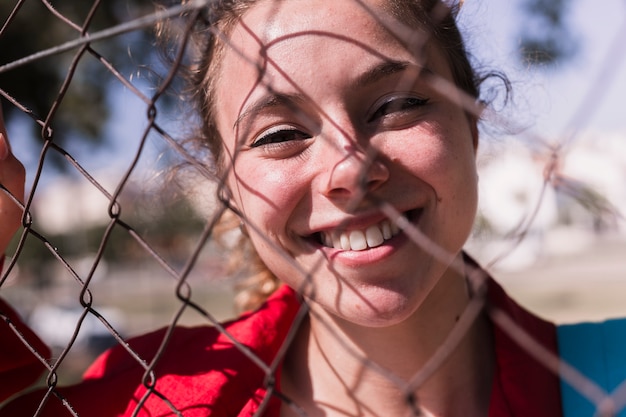 Cara de la muchacha sonriente joven que se coloca detrás de rejilla