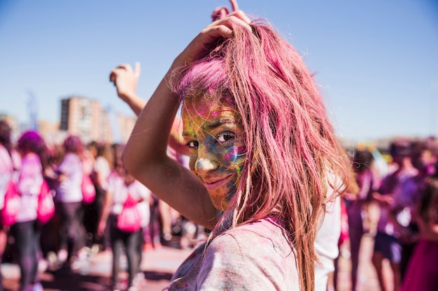 La cara de la mujer joven cubierta con polvo holi mirando a la cámara