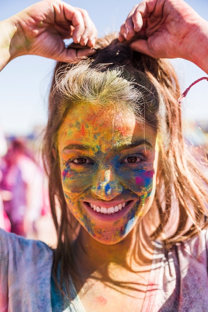 La cara de la mujer joven sonriente cubierta con el color de Holi que mira la cámara