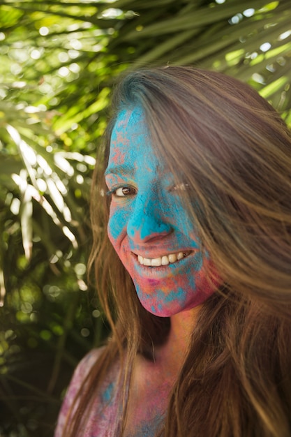 La cara de la mujer joven sonriente cubierta con el color de Holi que mira la cámara