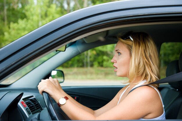 Cara de perfil de mujer asustada sentada en el coche y sostiene el volante - al aire libre