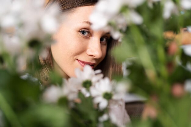 Cara sonriente de una hermosa joven rodeada de flores blancas y hojas verdes