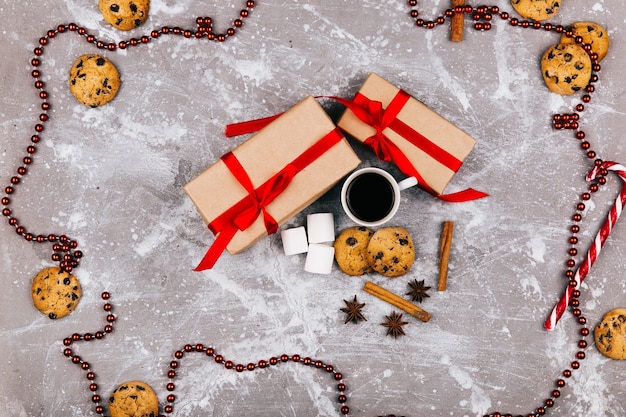 Caramelos blancos rojos, galletas, malvavisco, taza de café y presente cuadro se encuentran en el piso gris