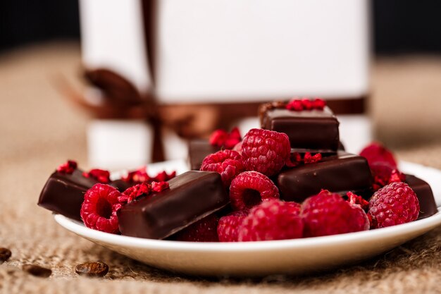 Caramelos de chocolate y frambuesa en plato blanco sobre tela de saco.