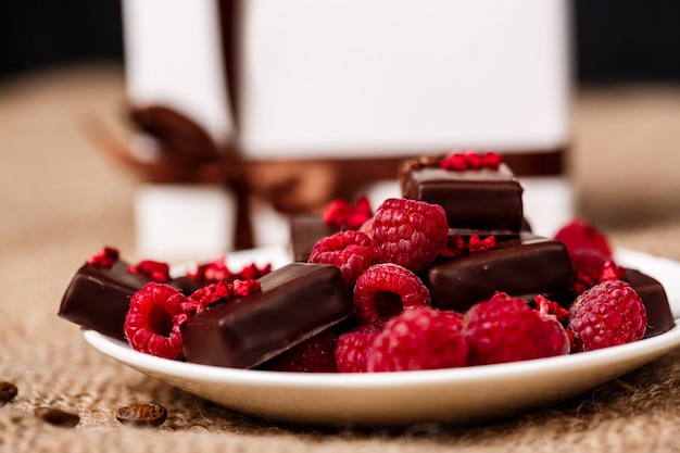 Caramelos de chocolate y frambuesa en plato blanco sobre tela de saco.