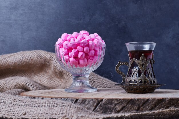 Caramelos de color rosa en una taza de vidrio con un vaso de té.