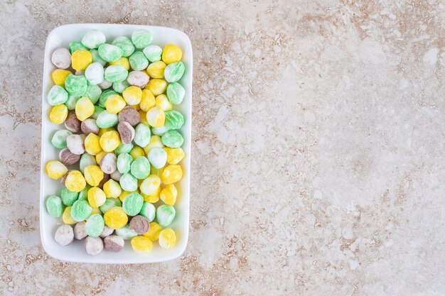 Caramelos de colores en un plato, sobre el mármol.