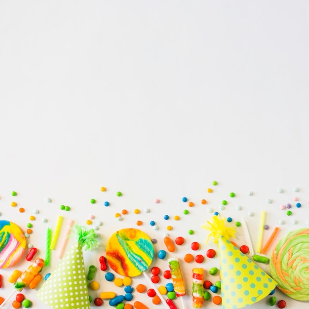 Foto gratuita caramelos de colores; velas y sombrero de fiesta sobre fondo blanco