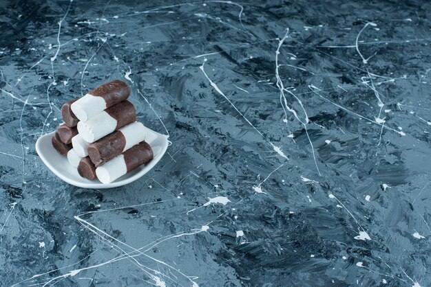 Caramelos de dos colores en un plato, sobre la mesa azul.