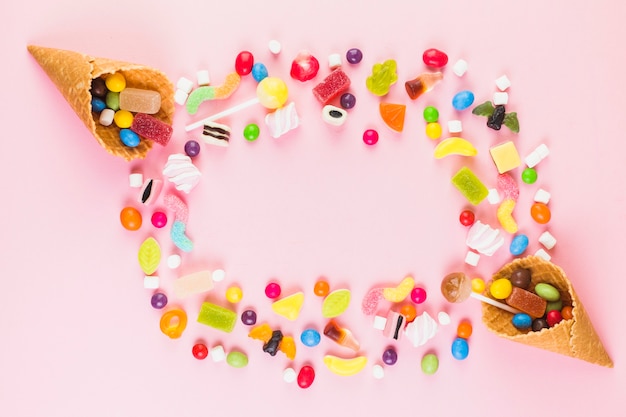 Caramelos dulces coloridos con dos helados cono de galleta en superficie rosa