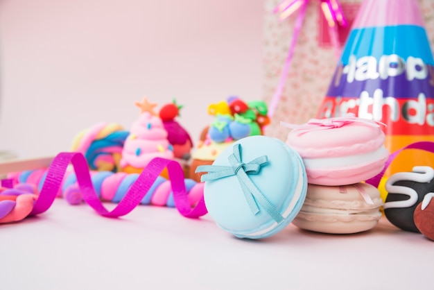 Caramelos dulces; macarrón; cintas y sombrero de cumpleaños en fondo rosa