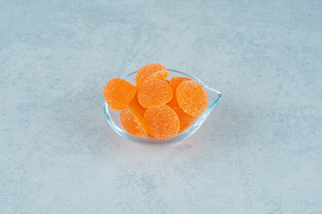 Caramelos de gelatina de naranja dulce con azúcar en una placa de vidrio sobre una superficie blanca