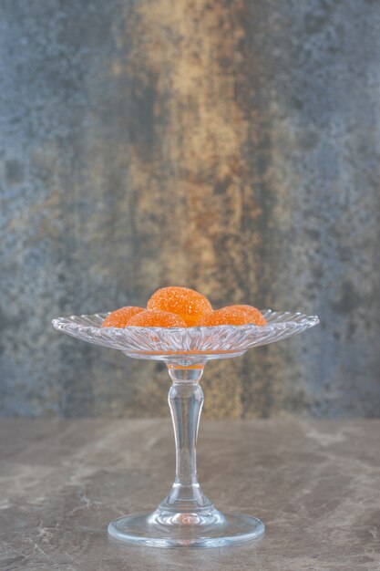 Foto gratuita caramelos de gelatina de naranja sobre el azucarero en la pared gris. foto vertical.