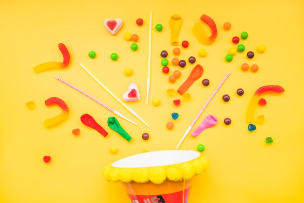 Foto gratuita caramelos de gelatina y velas sobre el sombrero de fiesta sobre fondo amarillo