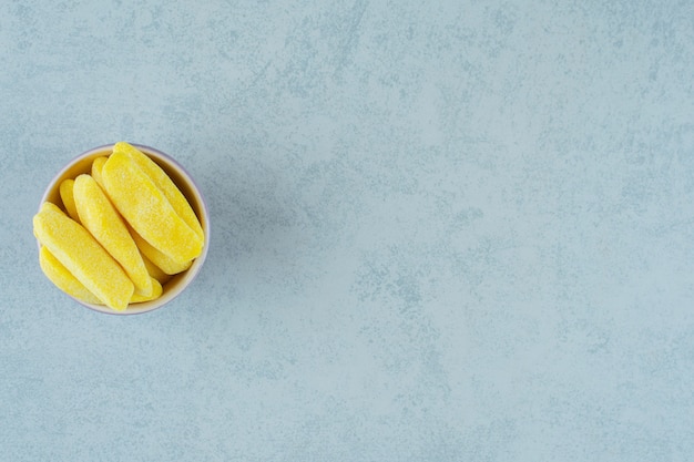 Caramelos para masticar con forma de plátano en un tazón sobre superficie blanca