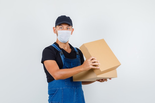 Cargador joven con caja de cartón abierta en uniforme, vista frontal de la máscara.