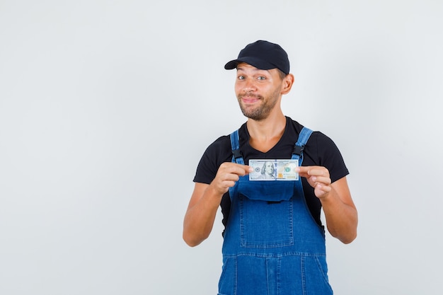 Foto gratuita cargador joven que sostiene el billete de un dólar en uniforme y que parece alegre. vista frontal.