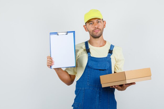 Cargador joven en uniforme con caja de cartón y portapapeles, vista frontal.