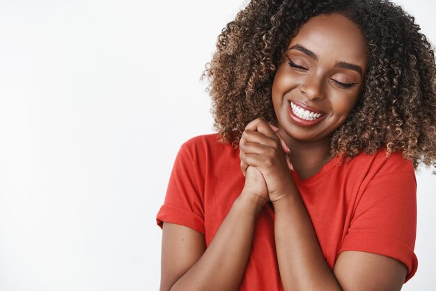 Cariñosa y cariñosa novia afroamericana agradecida por el novio romántico cerrar los ojos y sonreír ampliamente presionando las manos juntas felizmente