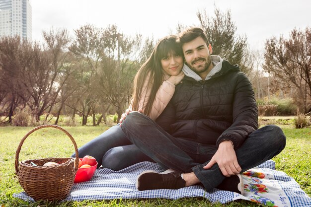 Cariñosa pareja joven sentada en una manta en el parque