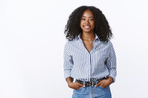 Carismática alegre atractiva mujer afroamericana corte de pelo rizado con camisa tomados de la mano bolsillos seguros salientes sonriendo, hablando conversación agradable, sintiéndose seguro de sí mismo relajado