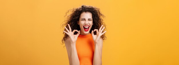 Foto gratuita carismática, feliz y alegre, atractiva mujer joven con peinado rizado que muestra buenos gestos con