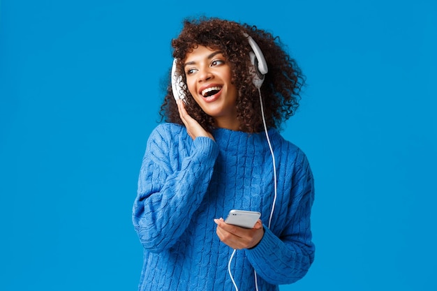 Carismática moderna joven atractiva chica afroamericana con corte de pelo afro escuchando música en los auriculares...