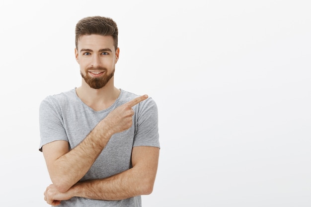 Carismático hombre de negocios encantado y seguro discutiendo el plan de negocios con el socio apuntando a la esquina superior derecha sonriendo complacido mostrando un buen lugar para copiar el espacio contra la pared blanca