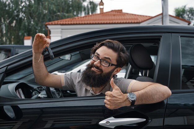 Carismático hombre sosteniendo las llaves del auto mostrando los pulgares para arriba