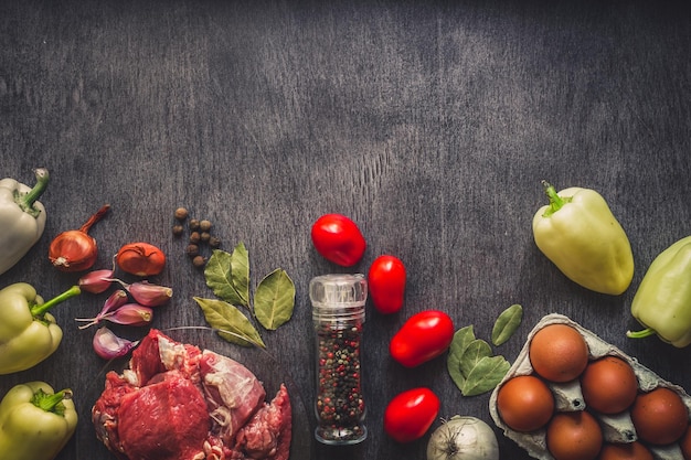 Carne de cerdo cruda sobre una superficie de madera oscura e ingredientes para cocinar. Fondo de alimentos con espacio de copia.