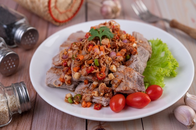 Carne de cerdo picante picada con tomate y lechuga en un plato blanco sobre una mesa de madera.