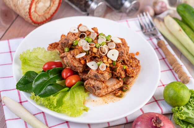 Carne de cerdo picante picada con tomate y lechuga en un plato blanco sobre una mesa de madera.