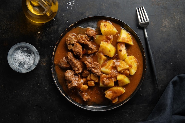 Carne con estofado de patata servido en plato sobre fondo oscuro